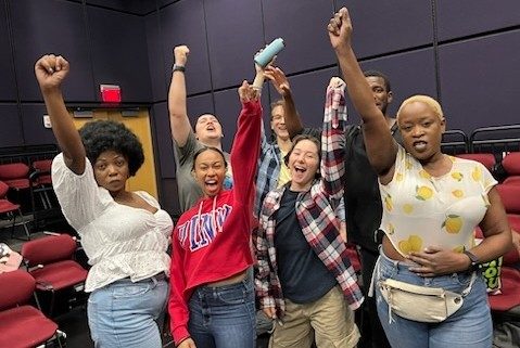 The cast of "Bits and Pieces" includes (front row, from left) Brenda Mselu, Bryanna Batts, Laurel Bennett, Dipo Katimba, (back row, from left) Kate Robbins, Jacob Takeshita, and Emmanuel Abuah, with arms raised in a fist.