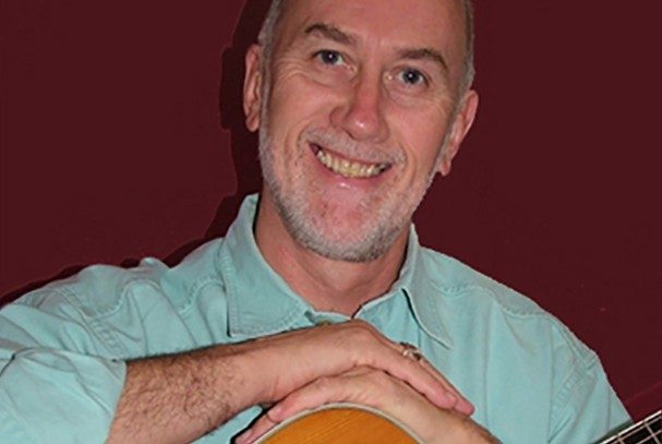 A man in an aqua shirt rests his hands on top of a guitar.