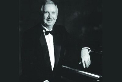 Pianist Robert Spillman is seated at a piano, dressed in a tuxedo.