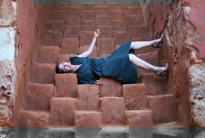 A sideways image of a woman wearing a blue dress standing against a wall made of large clay cubes