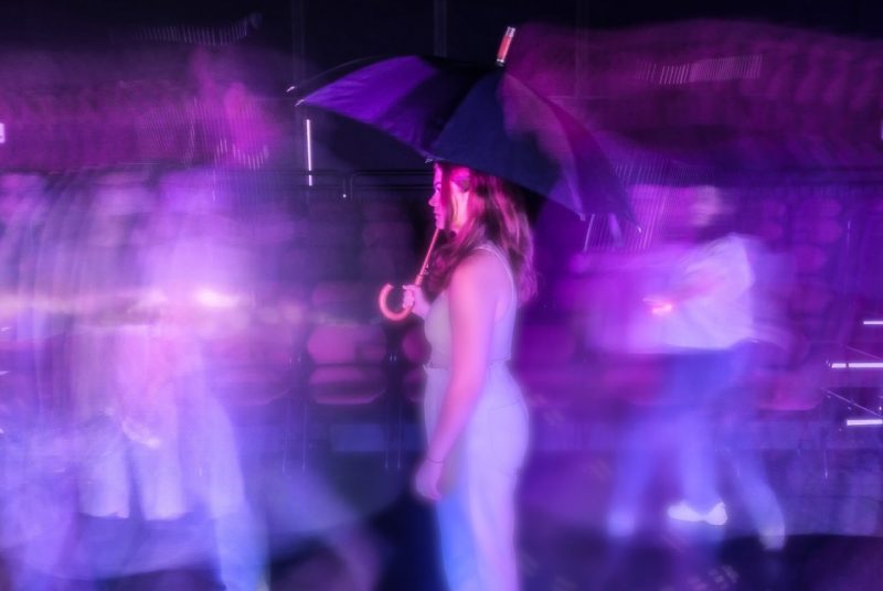 A purple-blue blurred image of a woman holding an umbrella, and other blurred images of people in the background.