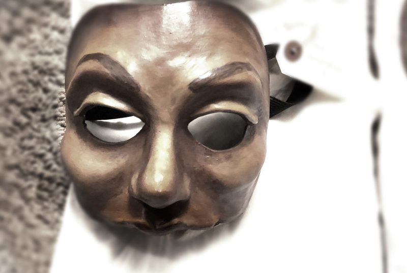 A bronze mask of a face sits on a white background