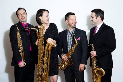 Four members of the h2 saxophone quartet, dressed in black with bright pink accents, each holding a saxophone.