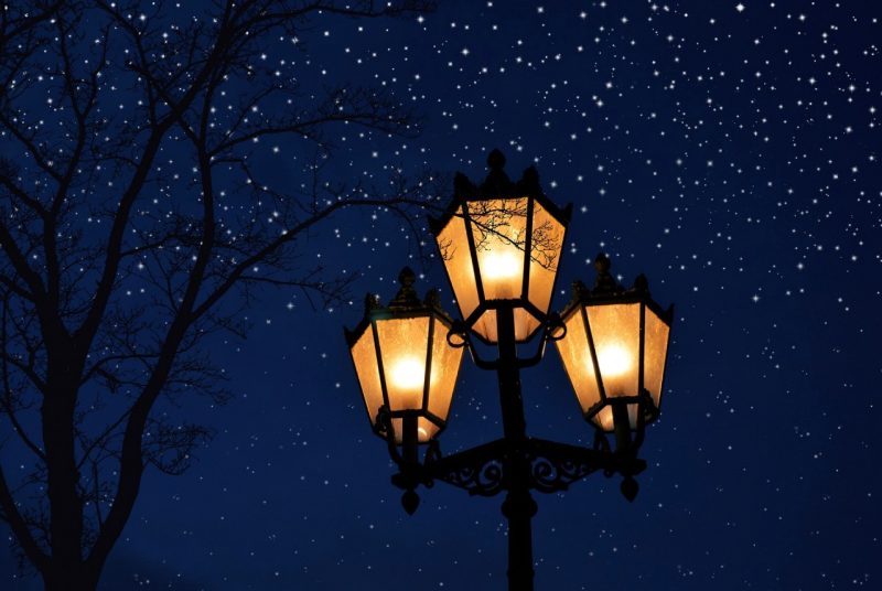 A lamp post of three lights, lit and glowing in a golden hue, against a dark, starry night