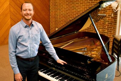 Pianist Peter Ryan stands in a studio with one hand on a grand piano