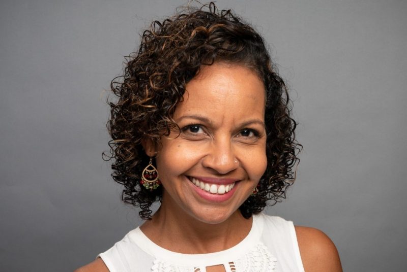 michelle ramos A woman with dark, short, curly hair, smiling, wearing a sleeveless white top