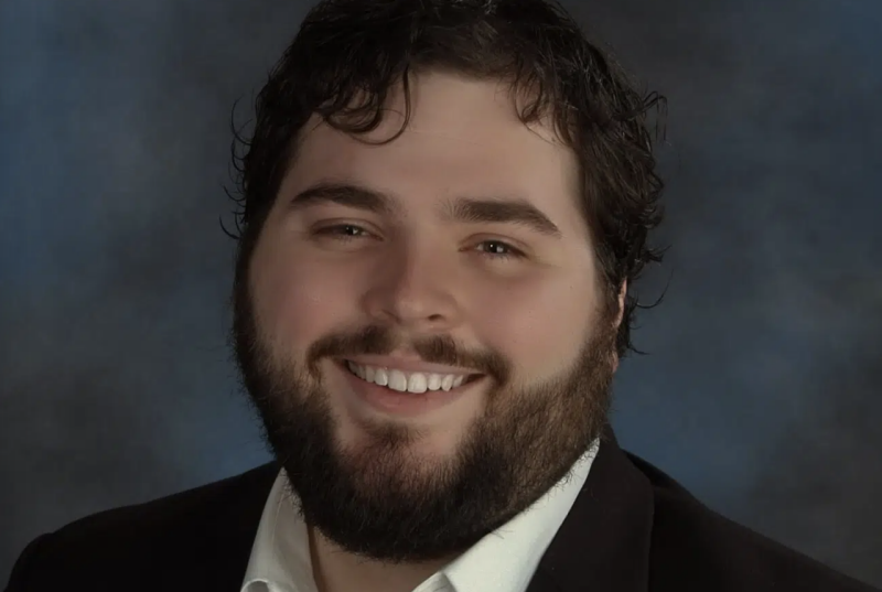 A headshot of tenor Jonathan Elmore, a man with dark hair, a short beard, smiling.