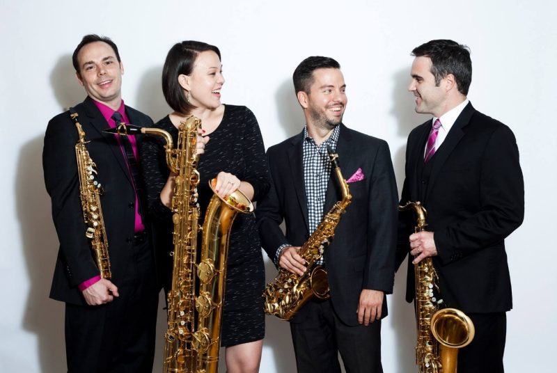 h2 quartet Four members of the h2 saxophone quartet, dressed in black with bright pink accents, each holding a saxophone.