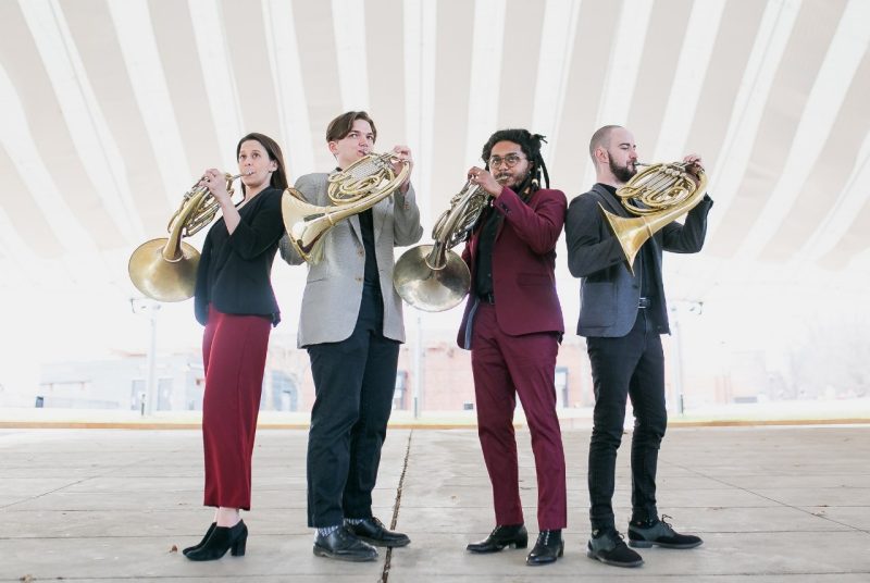 Four members of the Metropolitan Horn Authority, three men and one woman, play French horns